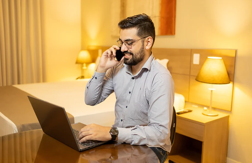 Agente de viagens trabalhando no Ville Hotel Gramadão em Votuporanga, com notebook e celular em ambiente corporativo confortável.