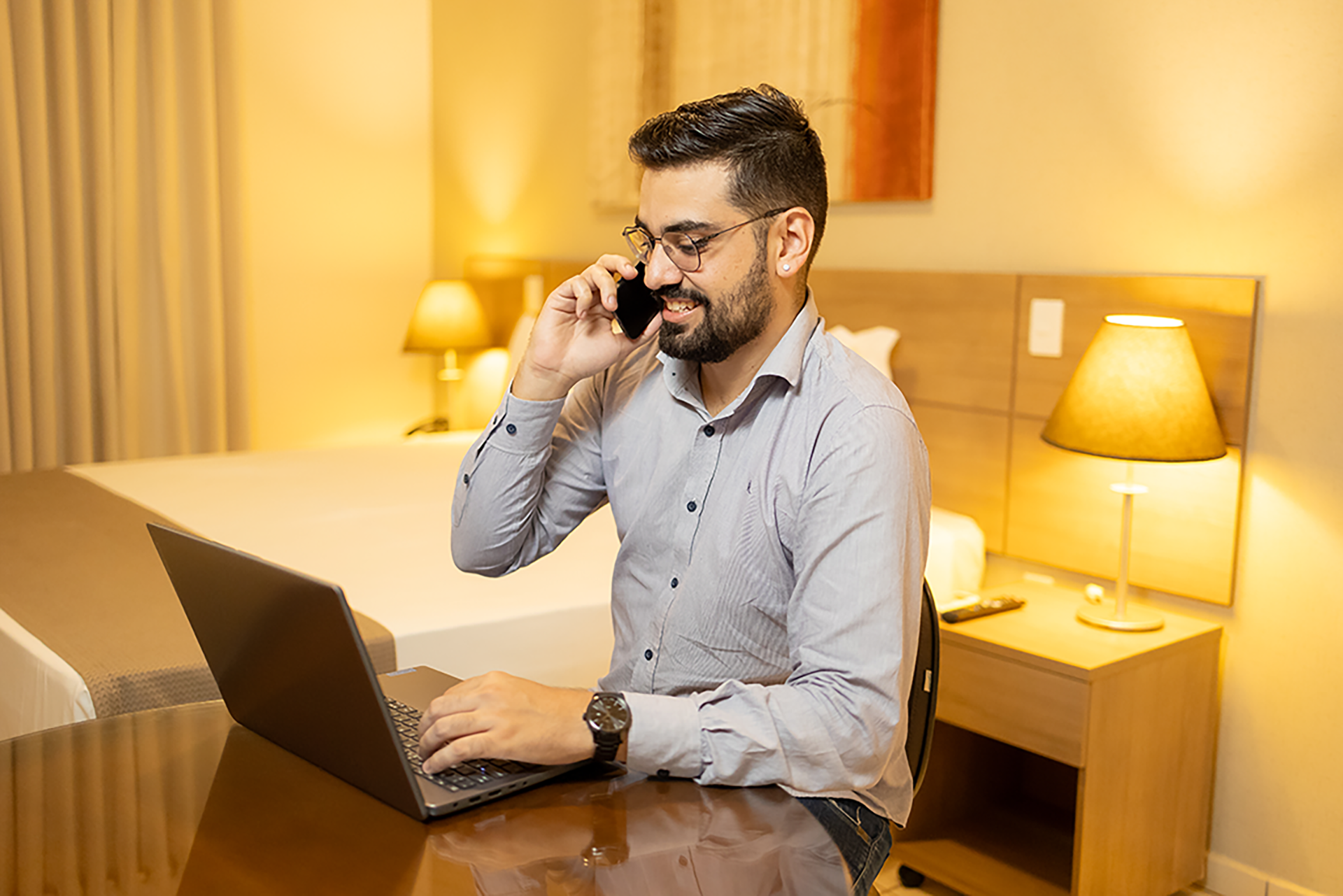 Agente de viagens trabalhando no Ville Hotel Gramadão em Votuporanga, com notebook e celular em ambiente corporativo confortável.