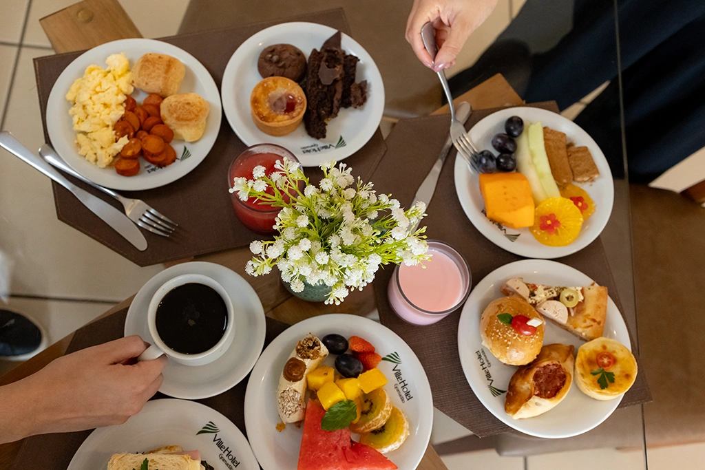 Mesa de café da manhã com pratos variados e sucos naturais no Ville Hotel Gramadão