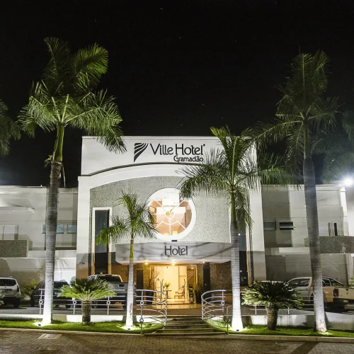 Fachada do Ville Hotel Gramadão em Votuporanga, com arquitetura moderna, iluminação noturna e entrada principal destacada.